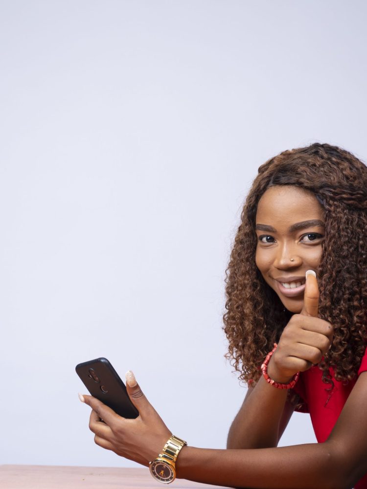 A beautiful black woman sitting sideways, holding her phone and a thumbs up
